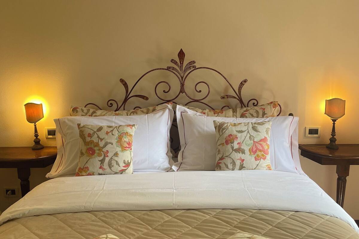 Una cama con cabecera estampada con motivos florales, dos mesitas de noche con lámparas y una colcha acolchada.
