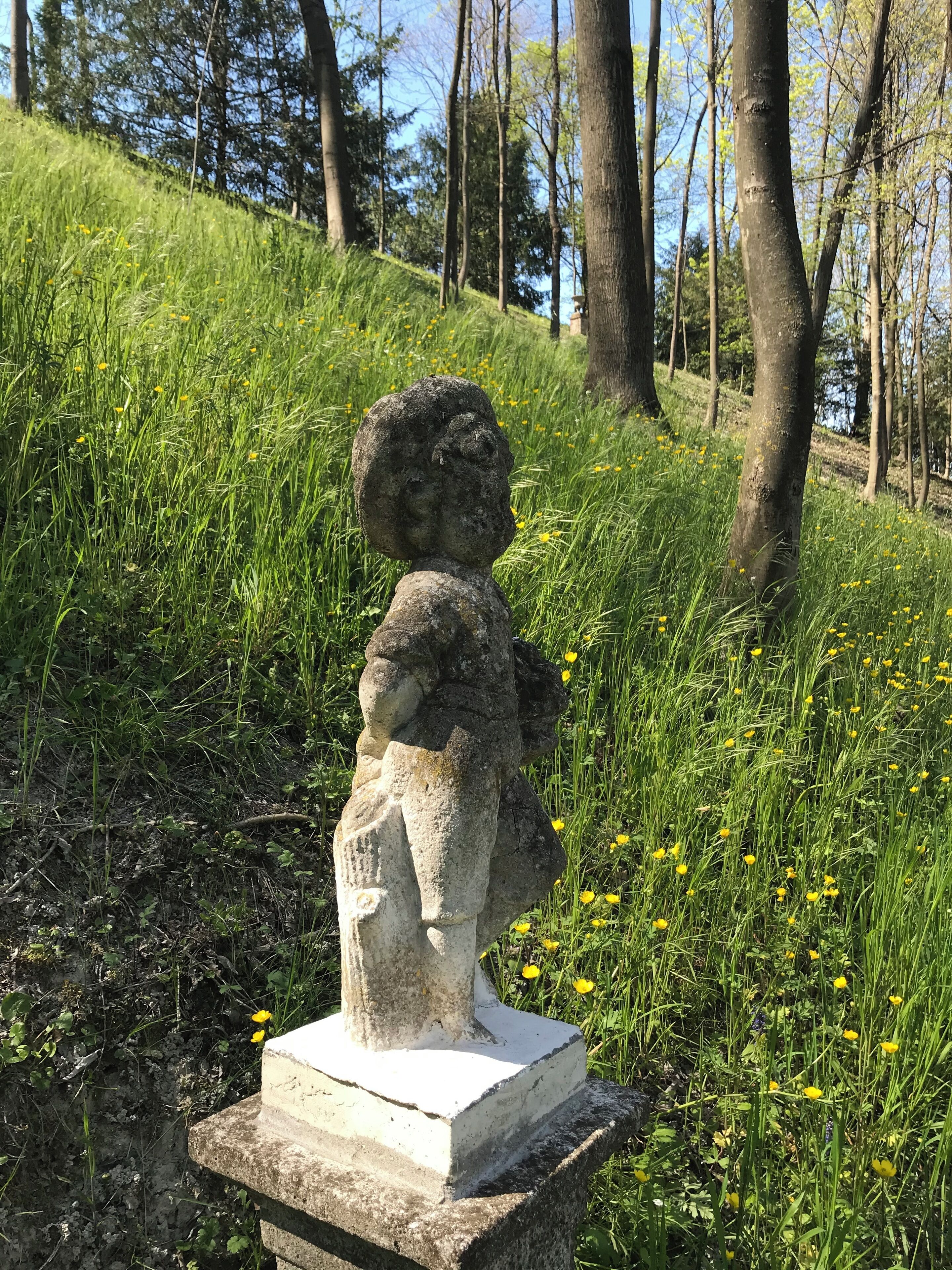 A stone statue of a child on a pedestal in a grassy area with trees in the background.