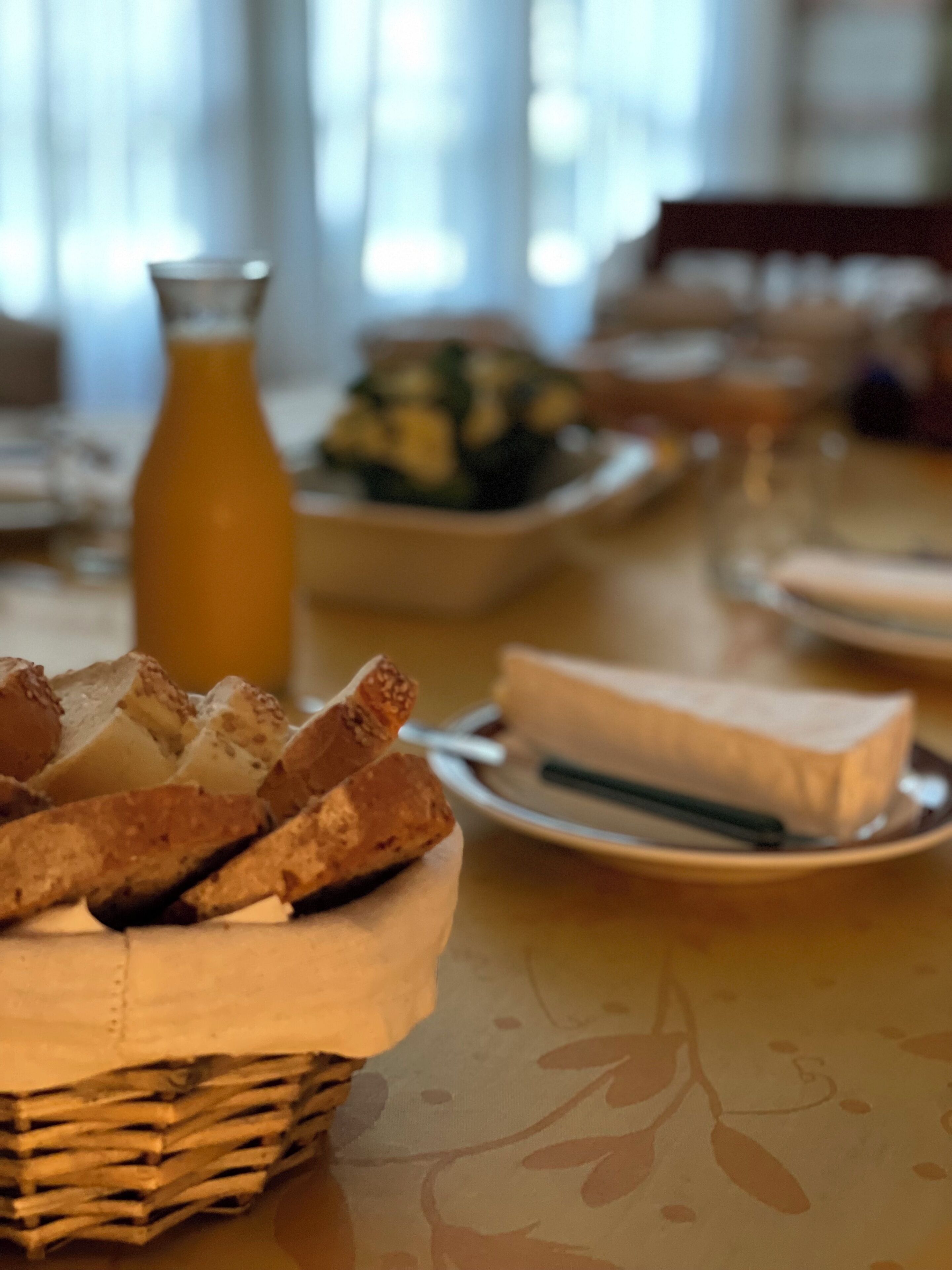 Ein Esstisch mit einem Korb voller Baguettes, einem Teller mit Käse und einer Flasche Orangensaft.