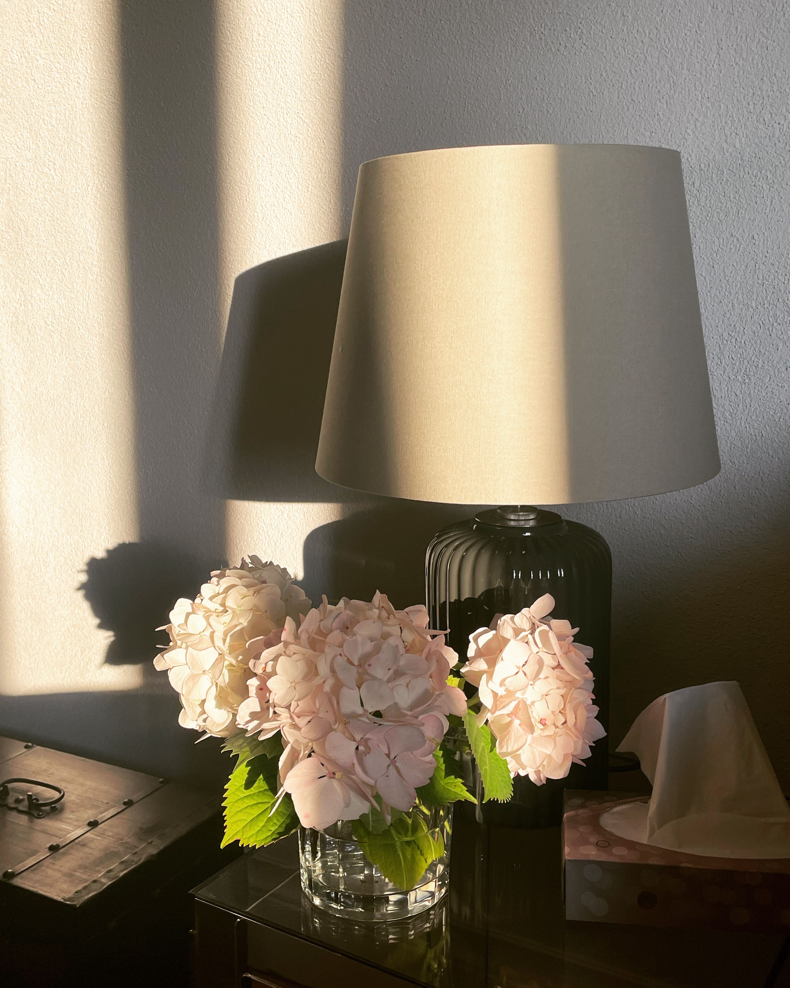 A lamp, a vase with flowers, and a tissue box on a table.