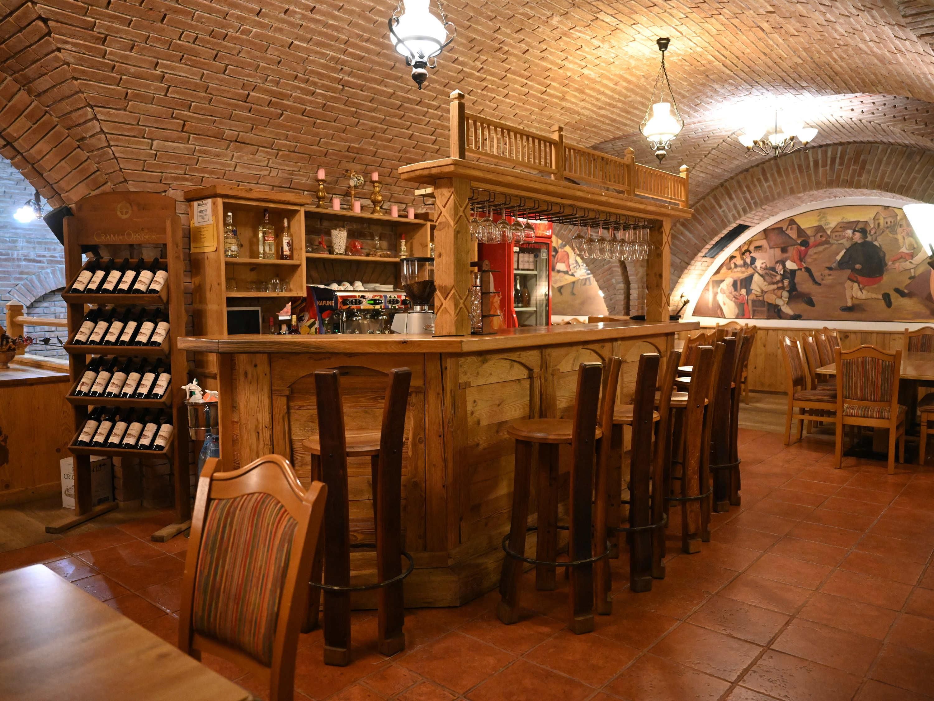 A rustic bar area with wooden shelves and stools, a brick ceiling, and a mural on the wall.