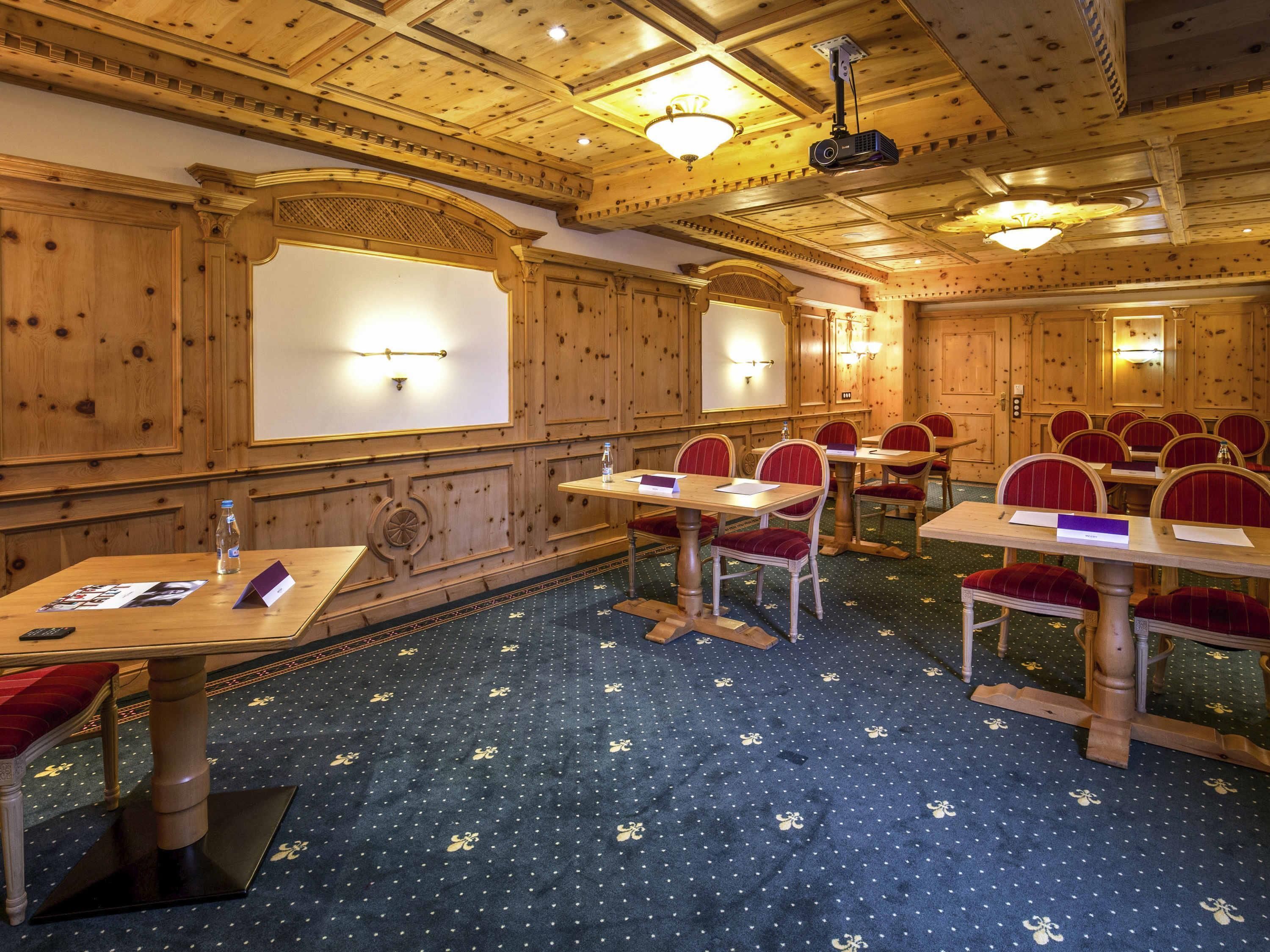 A conference room with wooden paneling, a projector, and tables with red upholstered chairs.