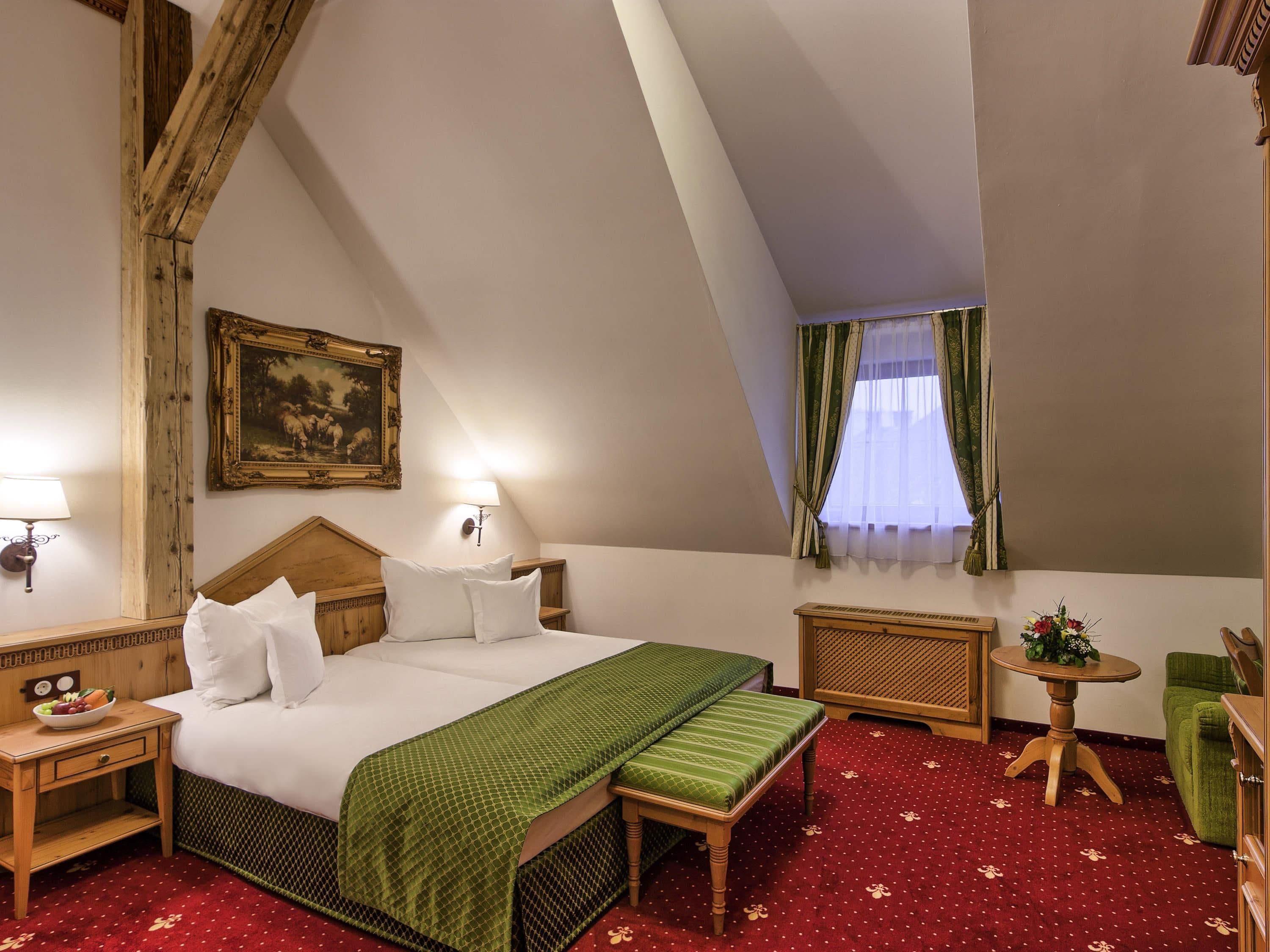 A hotel room with a large bed, a bench, a small table, a nightstand, and a picture on the wall.