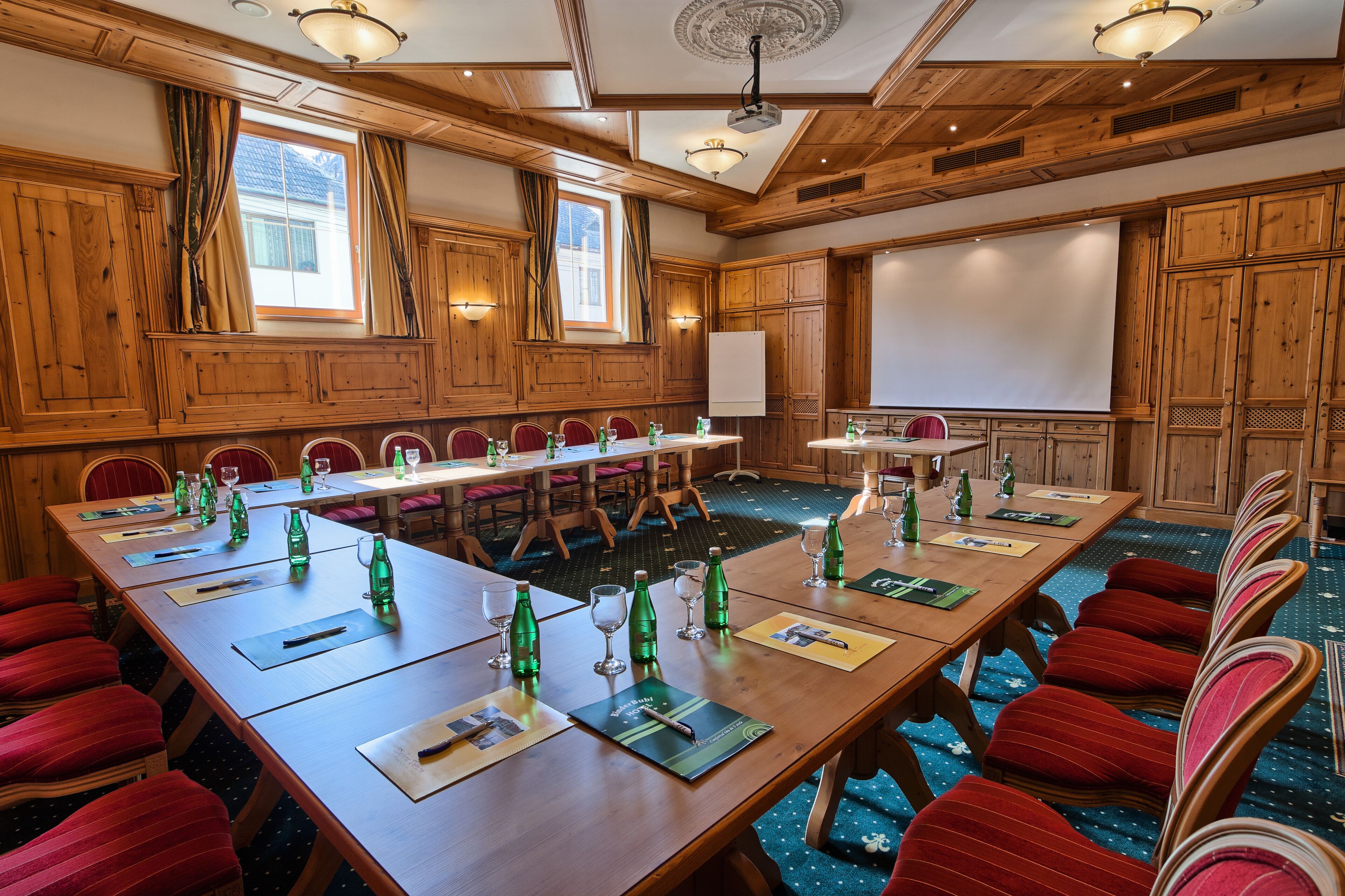 A conference room with wooden paneling, a large table with chairs, and a projector screen.