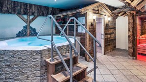 Un área de spa con jacuzzi, escalones de madera y una pared de piedra.
