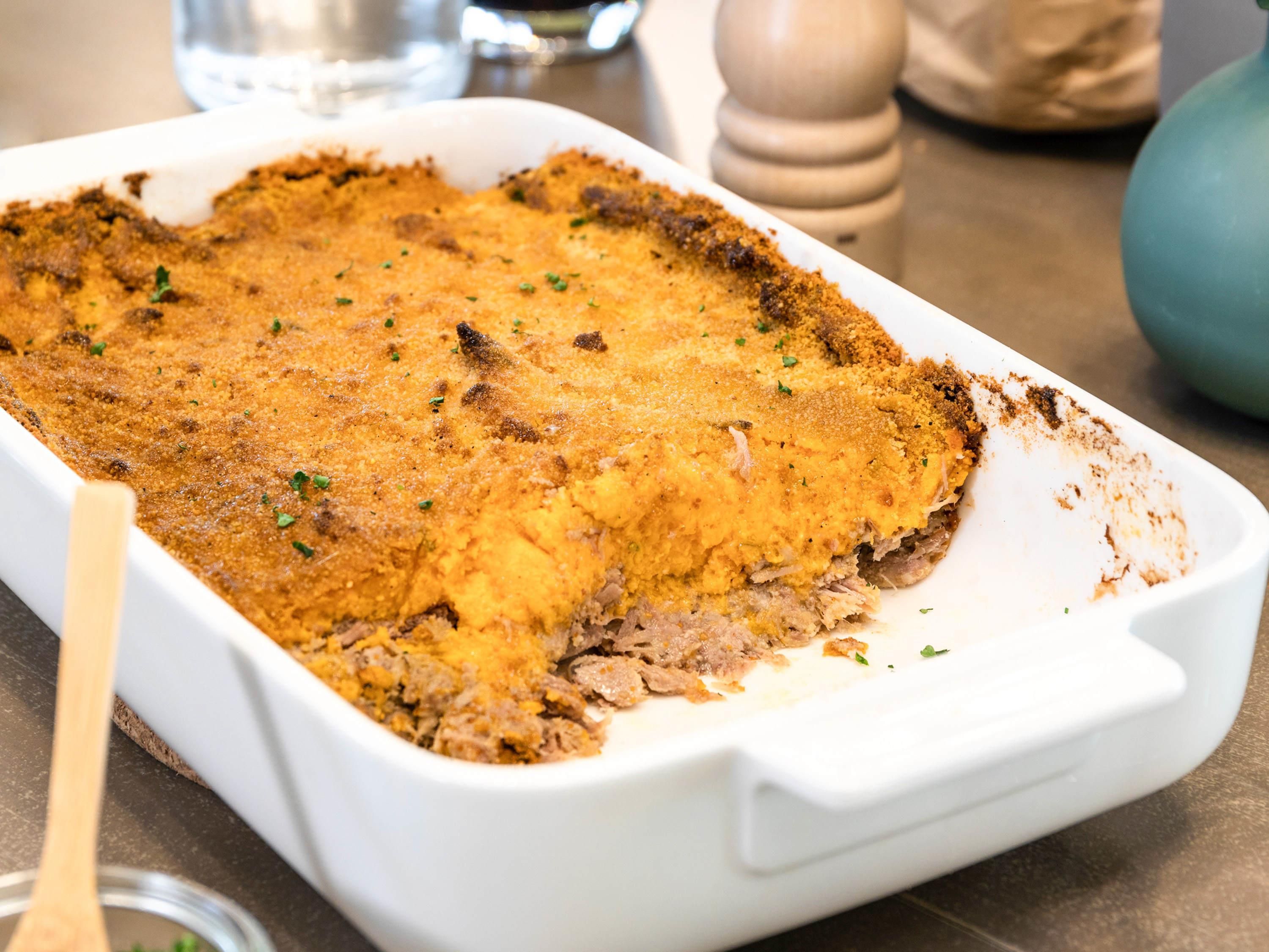 A white baking dish with a golden-brown crust, likely containing a meat-based dish, placed on a kitchen counter.