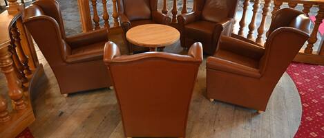 A circular seating area with a wooden table surrounded by four brown leather chairs, a wooden railing, and a red patterned carpet.