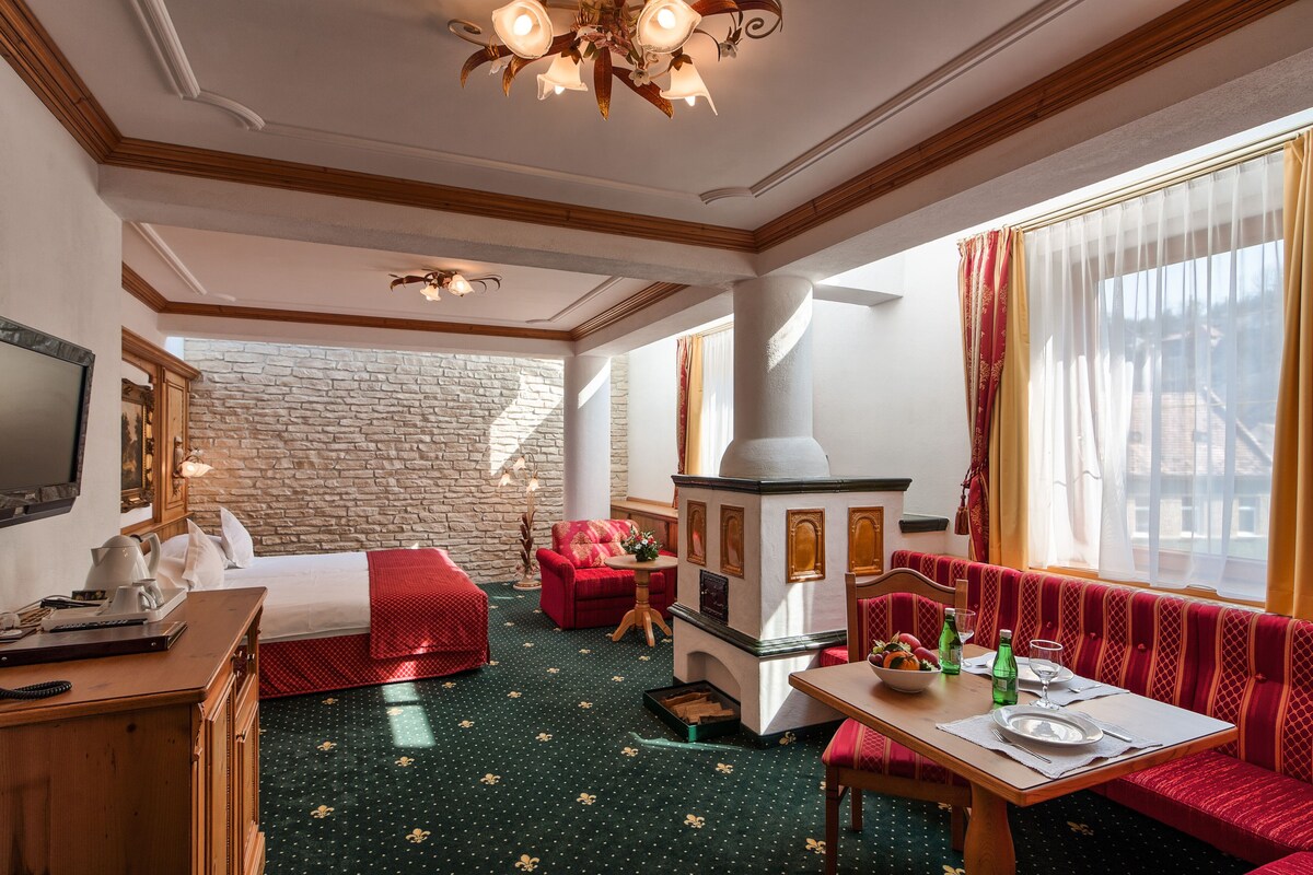 A hotel room with a stone wall, a fireplace, a bed, a sofa, and a dining area.