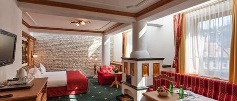 Habitación de hotel con pared de piedra, chimenea, cama, sofá y zona de comedor.