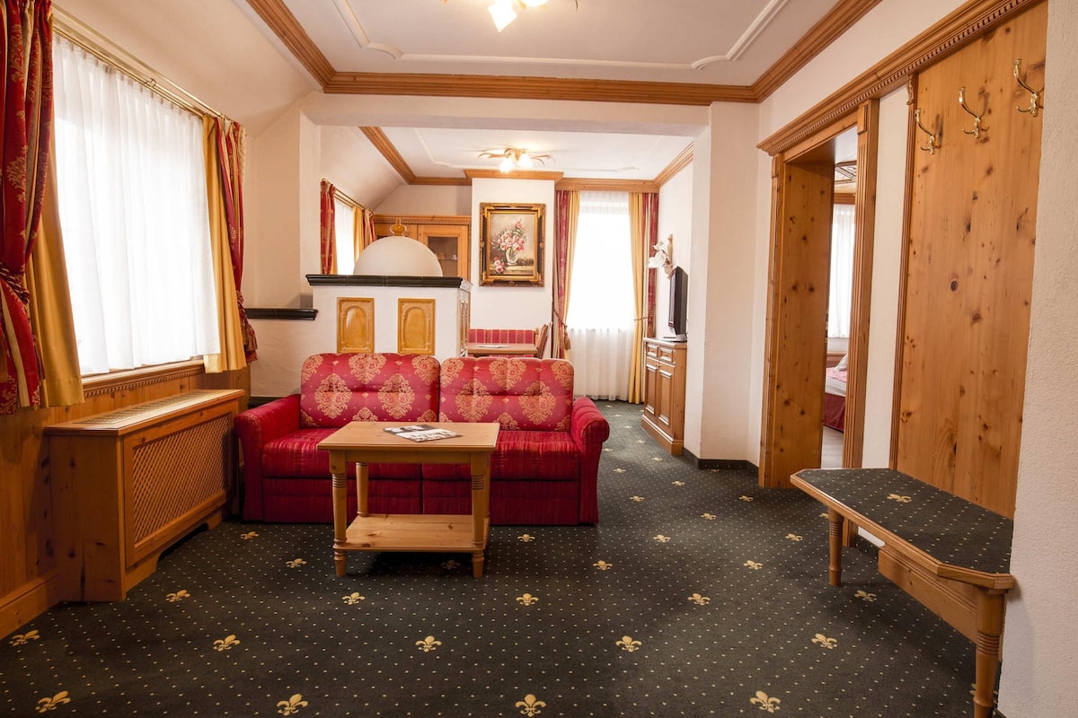 A room with a sofa, a small table, a wooden bench, a television, and a cabinet.