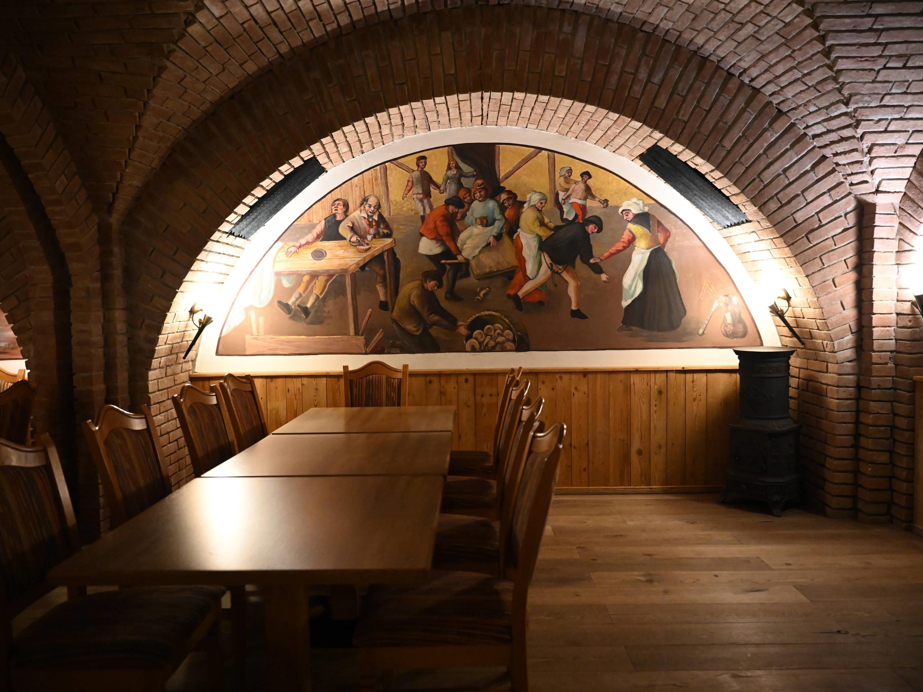A dining area with a long wooden table and chairs, a mural on the wall, and a brick arched ceiling.