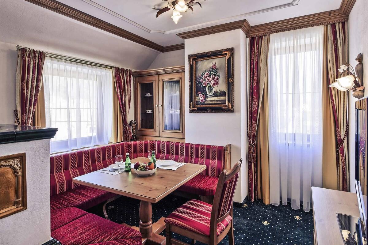 Une salle à manger avec une table en bois et des bancs recouverts d’un tissu rouge, un grand miroir et un tableau accroché au mur.