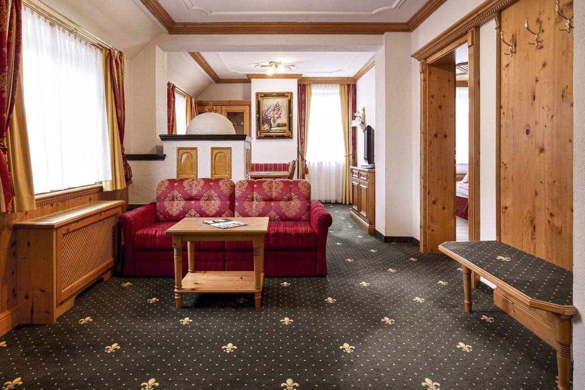 A room with a red sofa, a wooden table, and a bench. There is a wooden cabinet and a mirror on the wall.