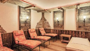 Un cuarto de spa con paredes de madera, una pared de piedra y una cama. Hay cuatro sillas y una mesita.