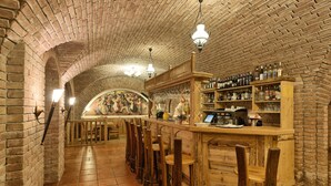 Zona de bar con paredes de ladrillo, taburetes de madera y estantes llenos de botellas y vasos.