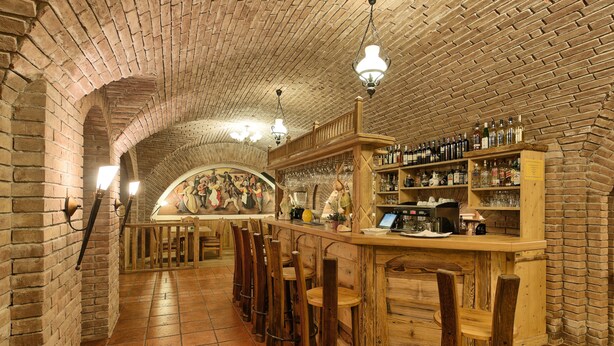 A bar area with brick walls, wooden bar stools, and shelves of bottles and glasses.