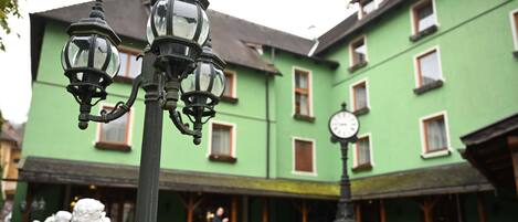 A courtyard with green buildings, outdoor seating, and a clock.