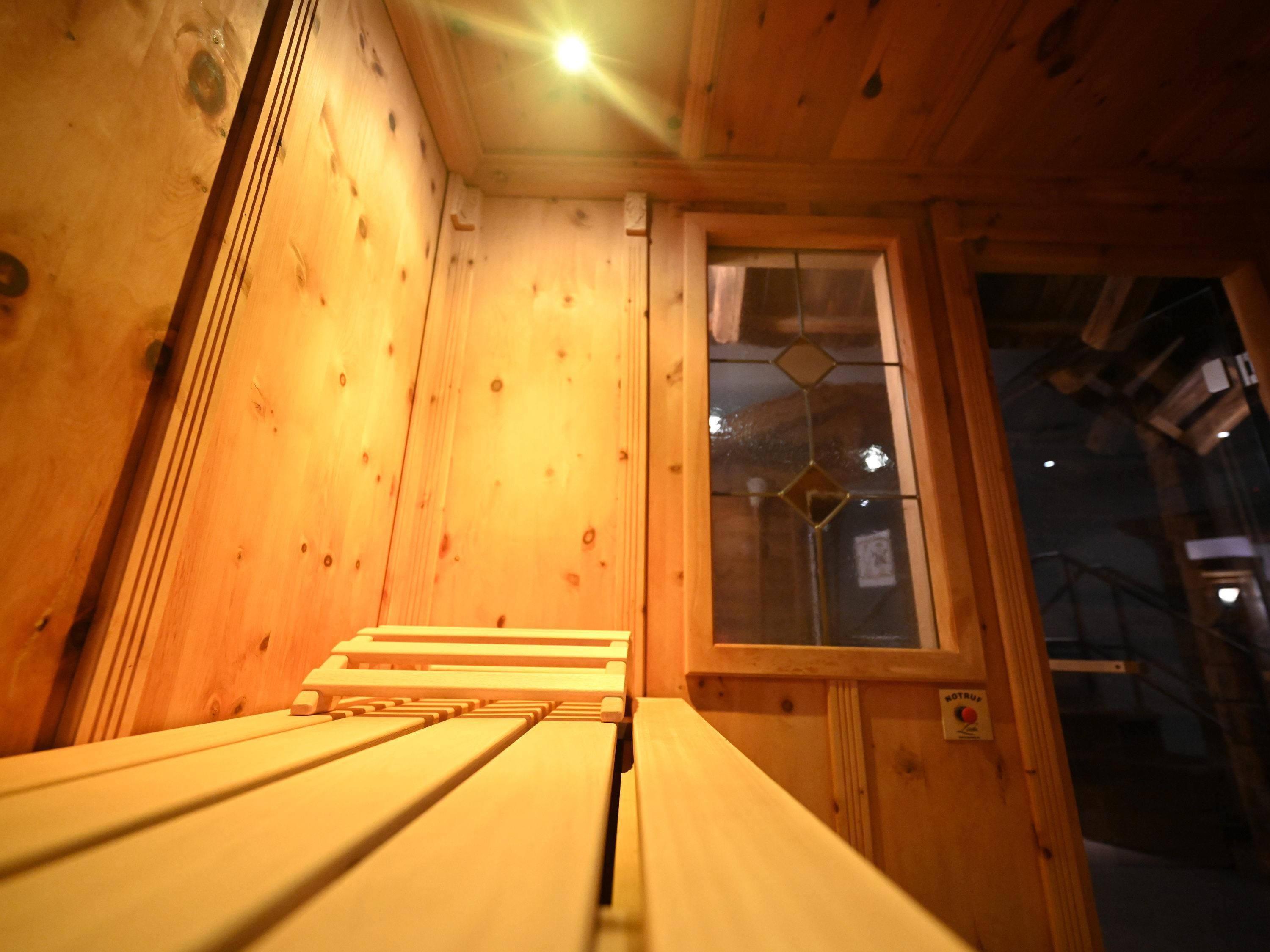 Un intérieur en bois avec un banc, une fenêtre ornée d’un motif géométrique et une porte avec une enseigne.