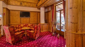 A wooden interior with a red patterned carpet, a sofa, and a television on the wall.