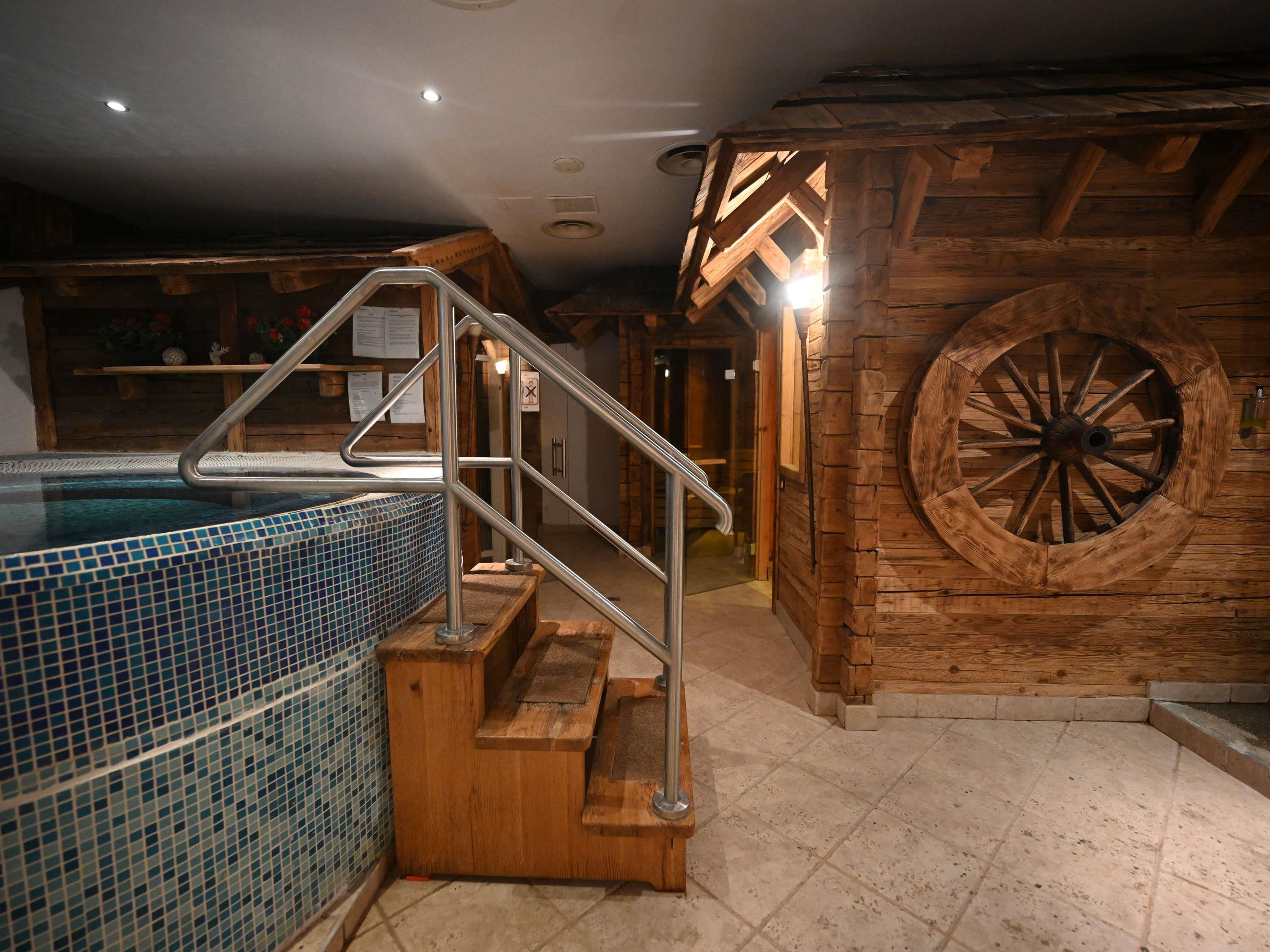 A wooden interior with a hot tub, metal stairs, and a large wooden wheel.