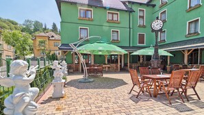Un espace extérieur aménagé en terrasse, avec un sol en briques, des tables et des chaises en bois, et des parasols verts.