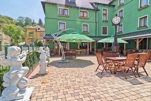 An outdoor patio area with brick flooring, wooden tables and chairs, and green umbrellas.