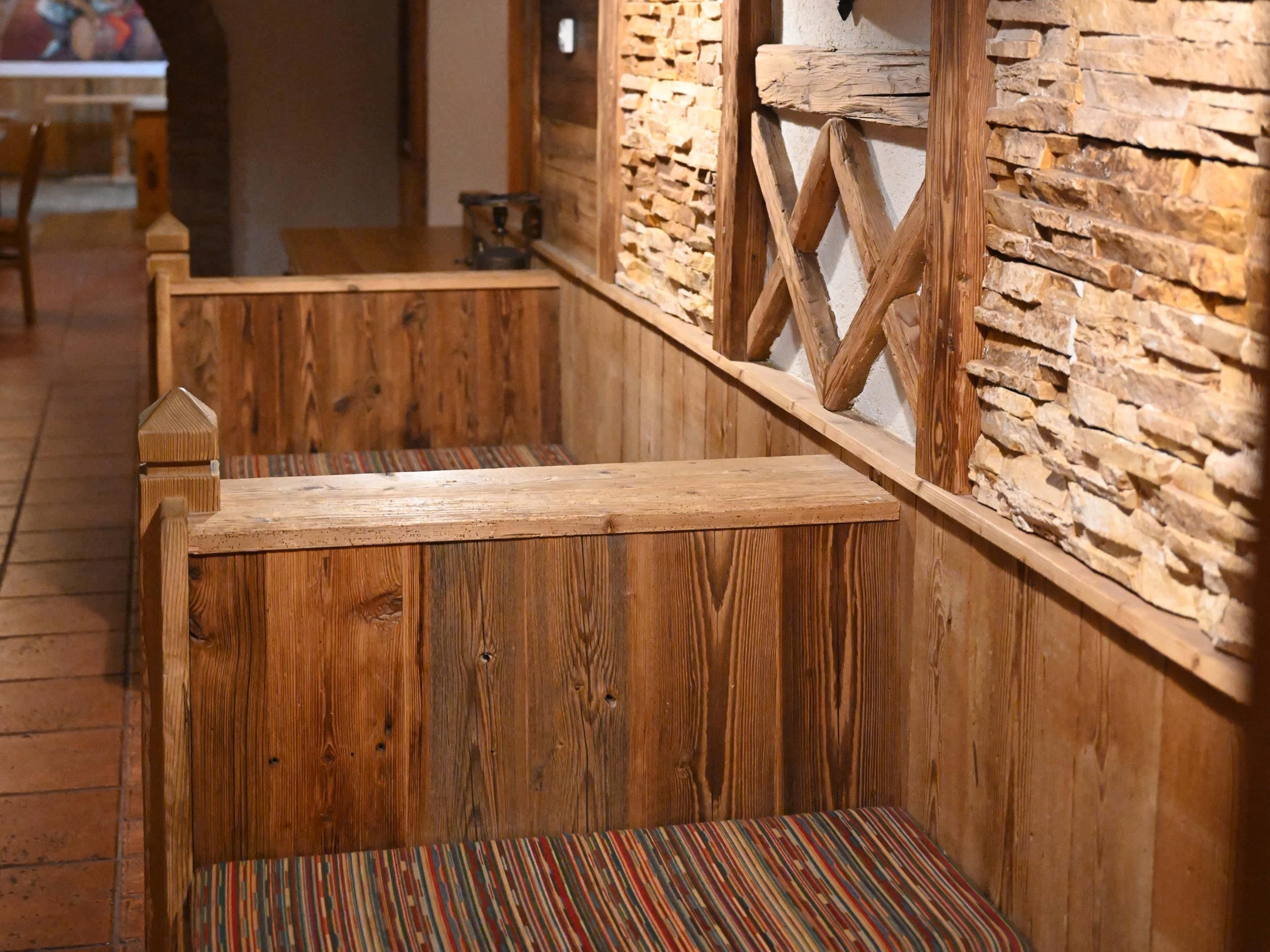 Un banco de madera con un cojín a rayas, una pared de piedra y una barandilla de madera.