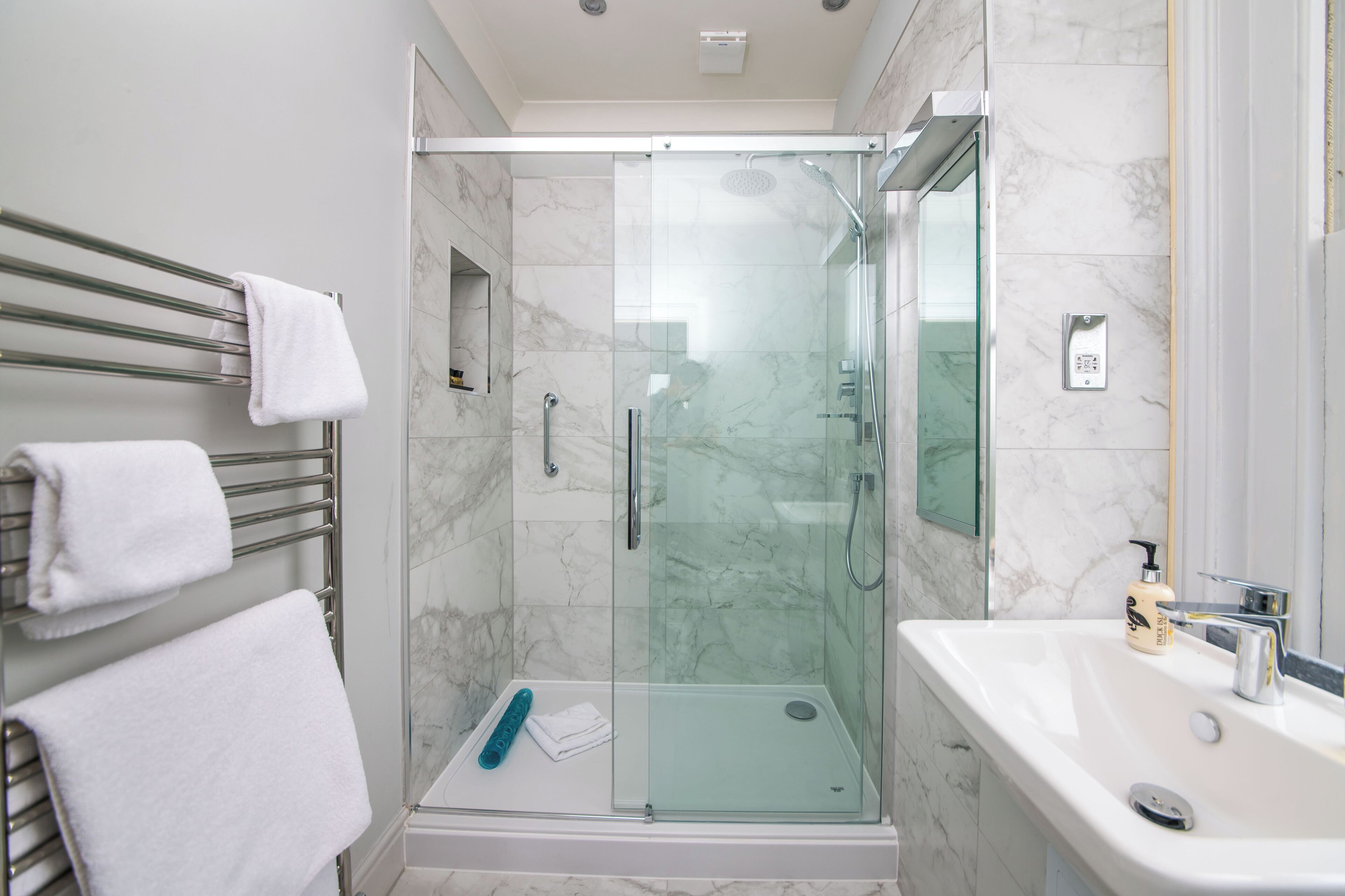 A modern bathroom with a glass-enclosed shower, a white sink, and a towel rack with white towels.