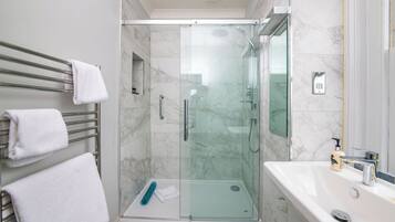 A modern bathroom with a glass-enclosed shower, a white sink, and a towel rack with white towels.