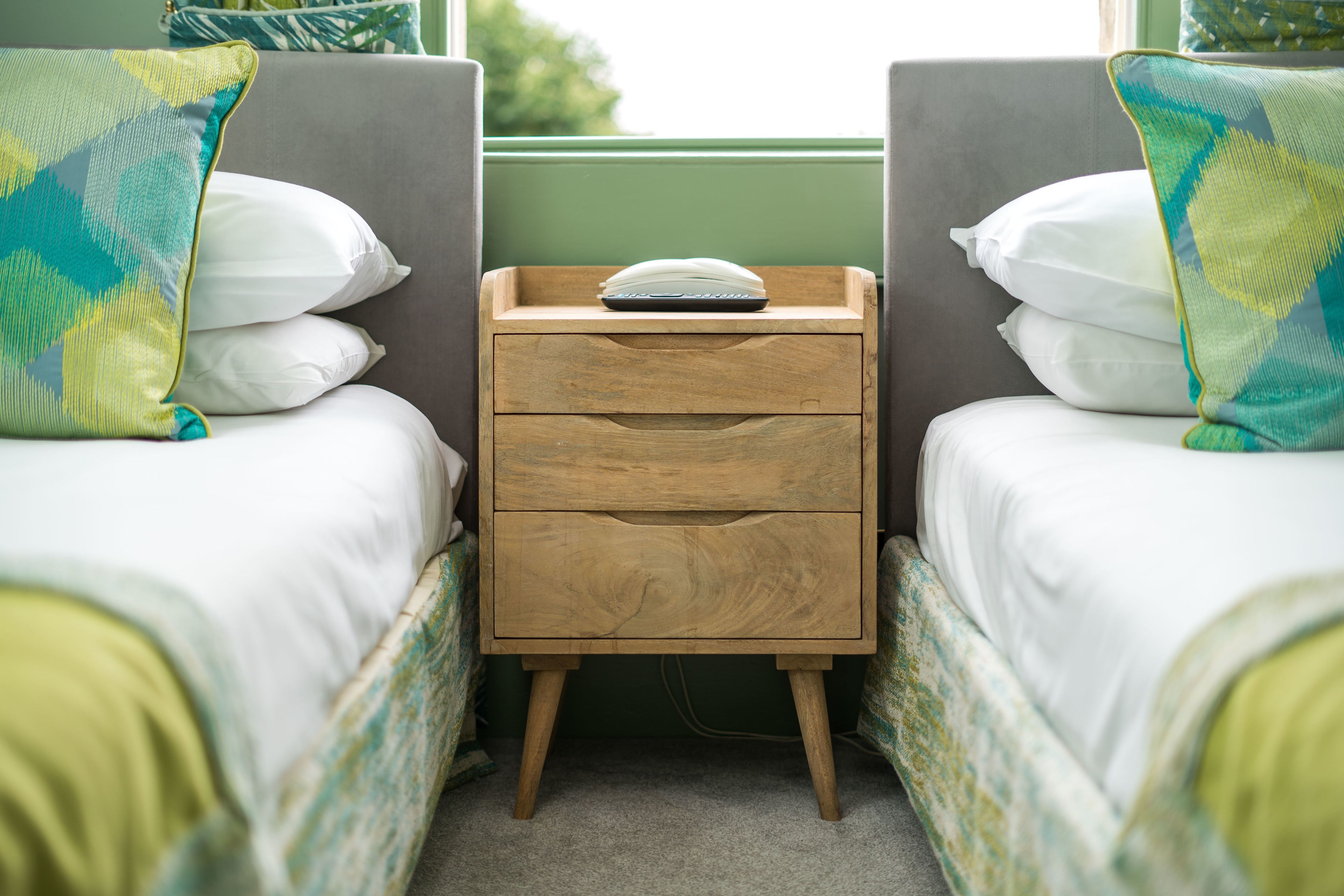 A small, cozy room with two single beds, each with a pillow and a small wooden nightstand between them.