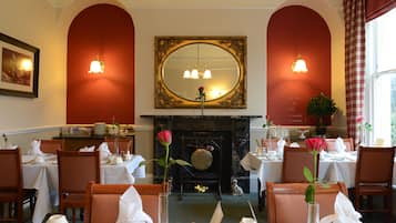 A dining area with tables set for service, a fireplace, and a large mirror above the mantel.