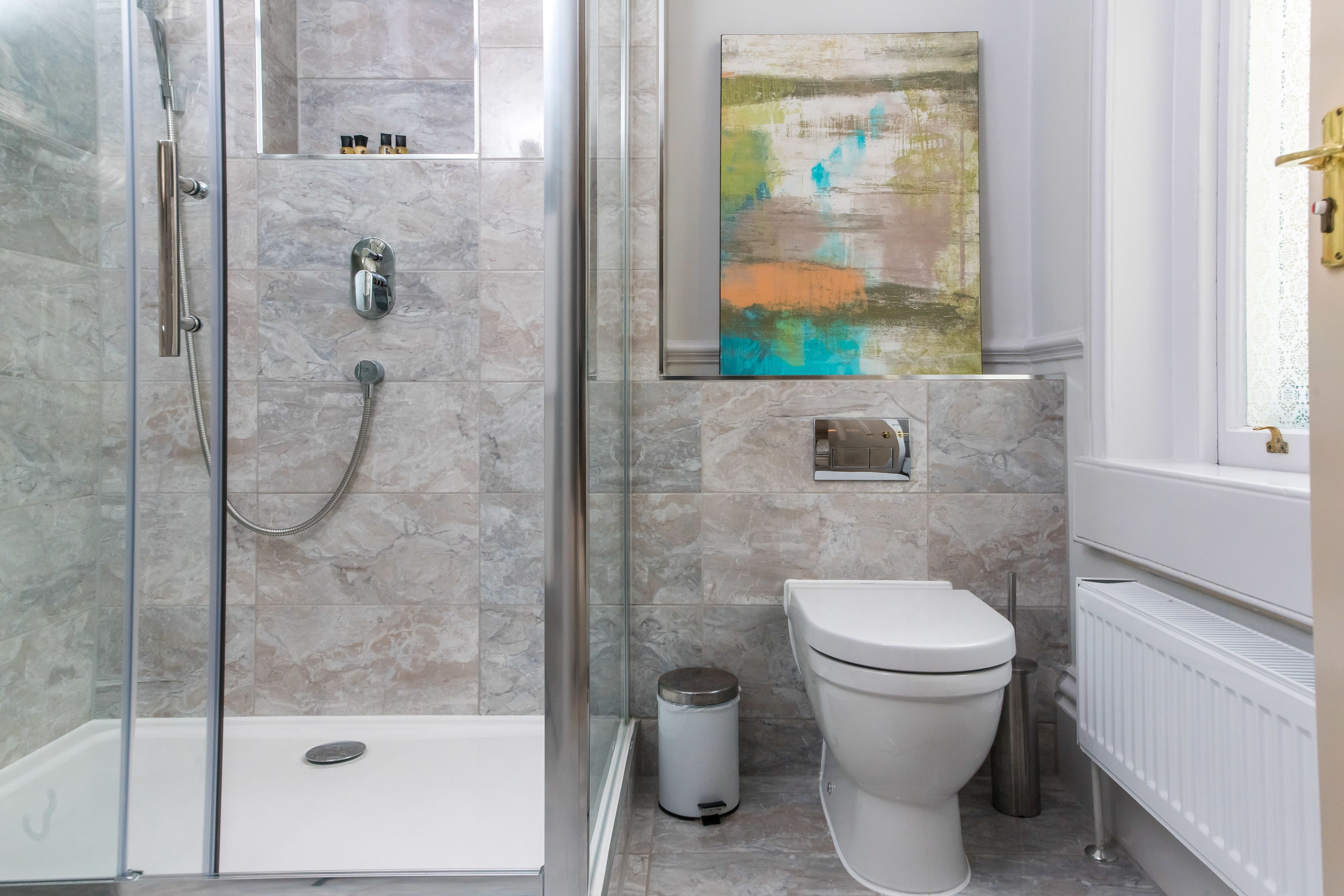A modern bathroom with a glass-enclosed shower, a toilet, and a radiator.