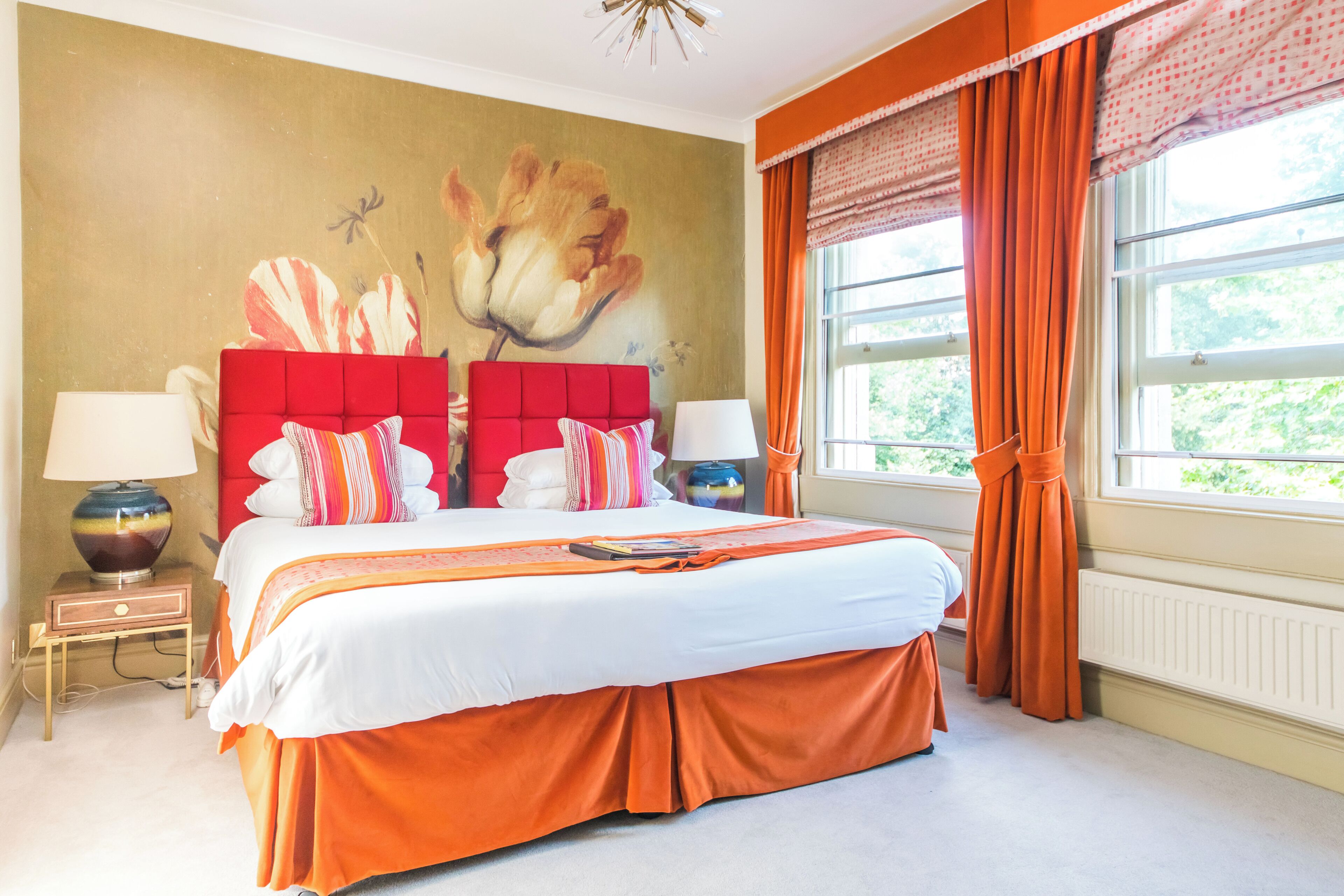 Un dormitorio con una cama grande, dos mesitas de noche, un mural en la pared y una ventana con cortinas.