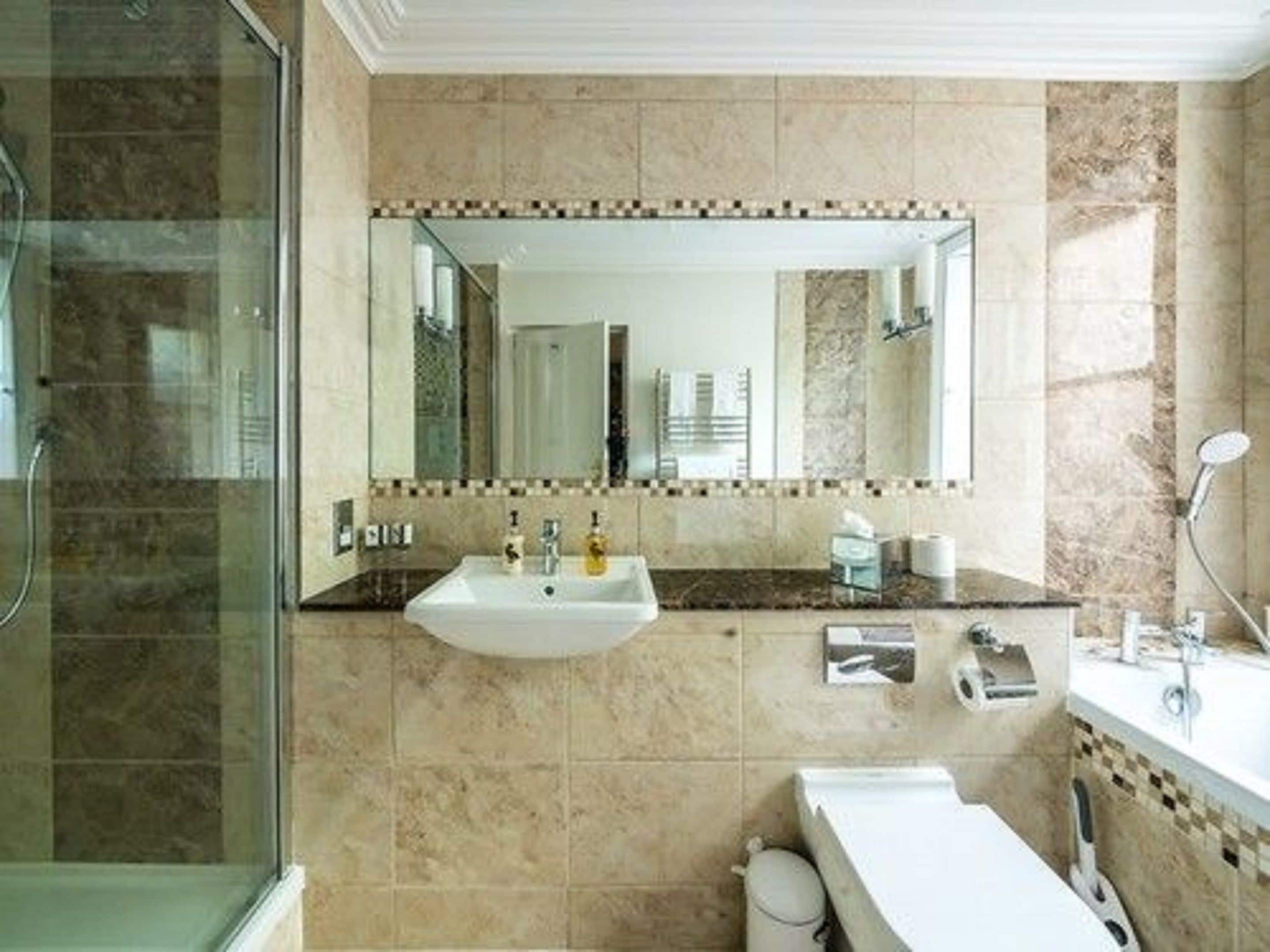 A bathroom with a large mirror, a sink, a shower, and a toilet.