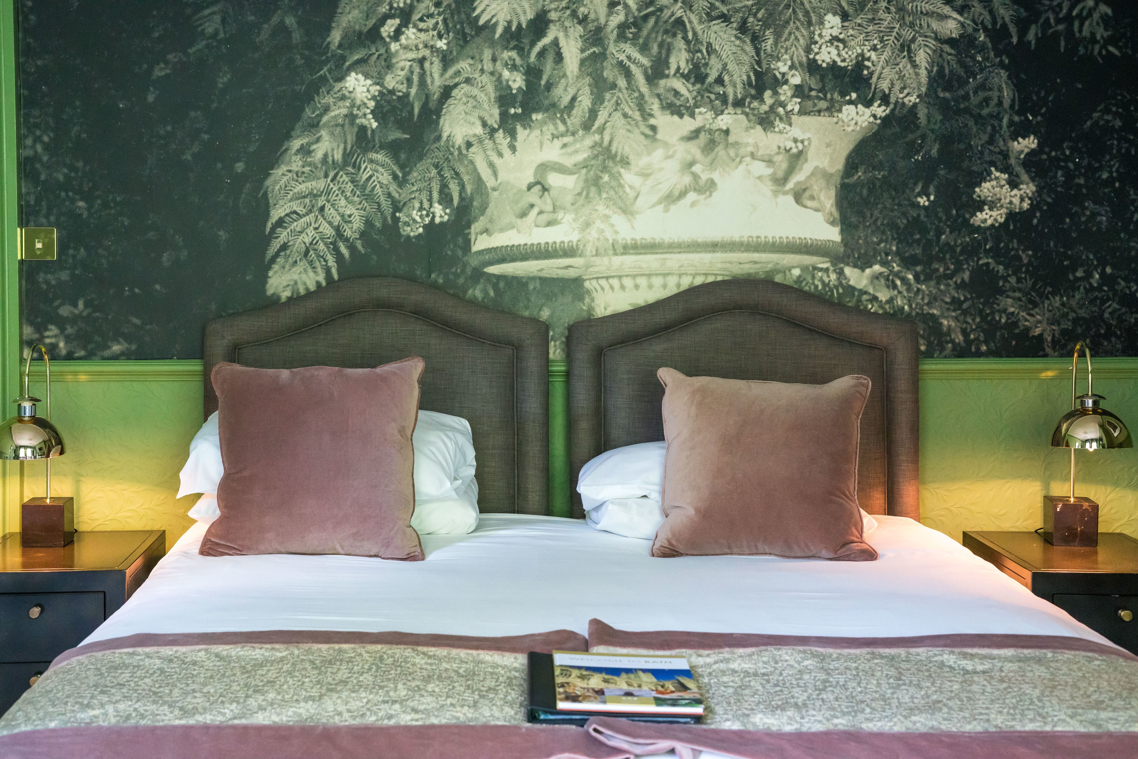 A double bed with two pillows, a nightstand with a lamp, and a wall mural.