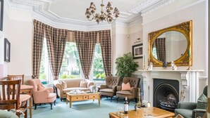A traditional living room with a fireplace, comfortable seating, and a large mirror. - The Ayrlington (Bath)