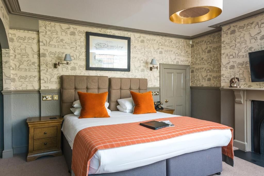 A bedroom with a large bed, two bedside tables, a framed picture on the wall, and a fireplace.
