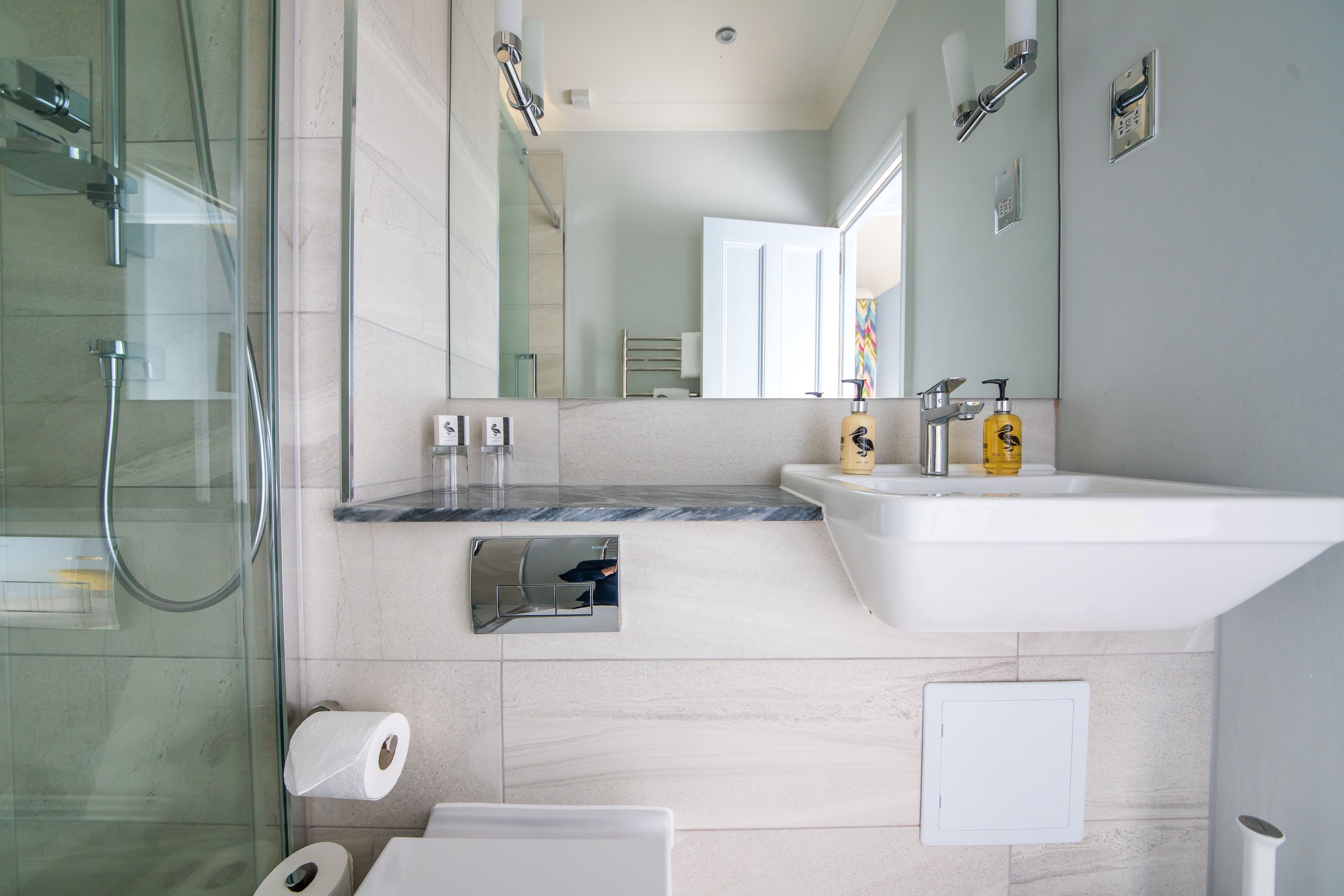 A modern bathroom with a glass shower enclosure, a marble countertop, a sink with a mirror, and a toilet.