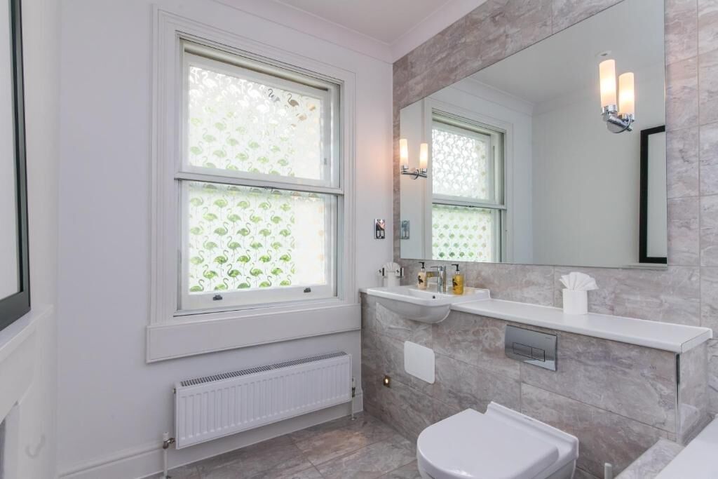 A bathroom with a window, a sink, a mirror, and a toilet.