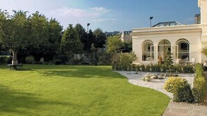A well-maintained lawn with a stone pathway leading to a building with arched windows. - The Ayrlington (Bath)