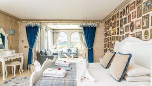 A hotel room with a large bed, a desk, a chair, and a wall adorned with framed pictures. - The Ayrlington (Bath)