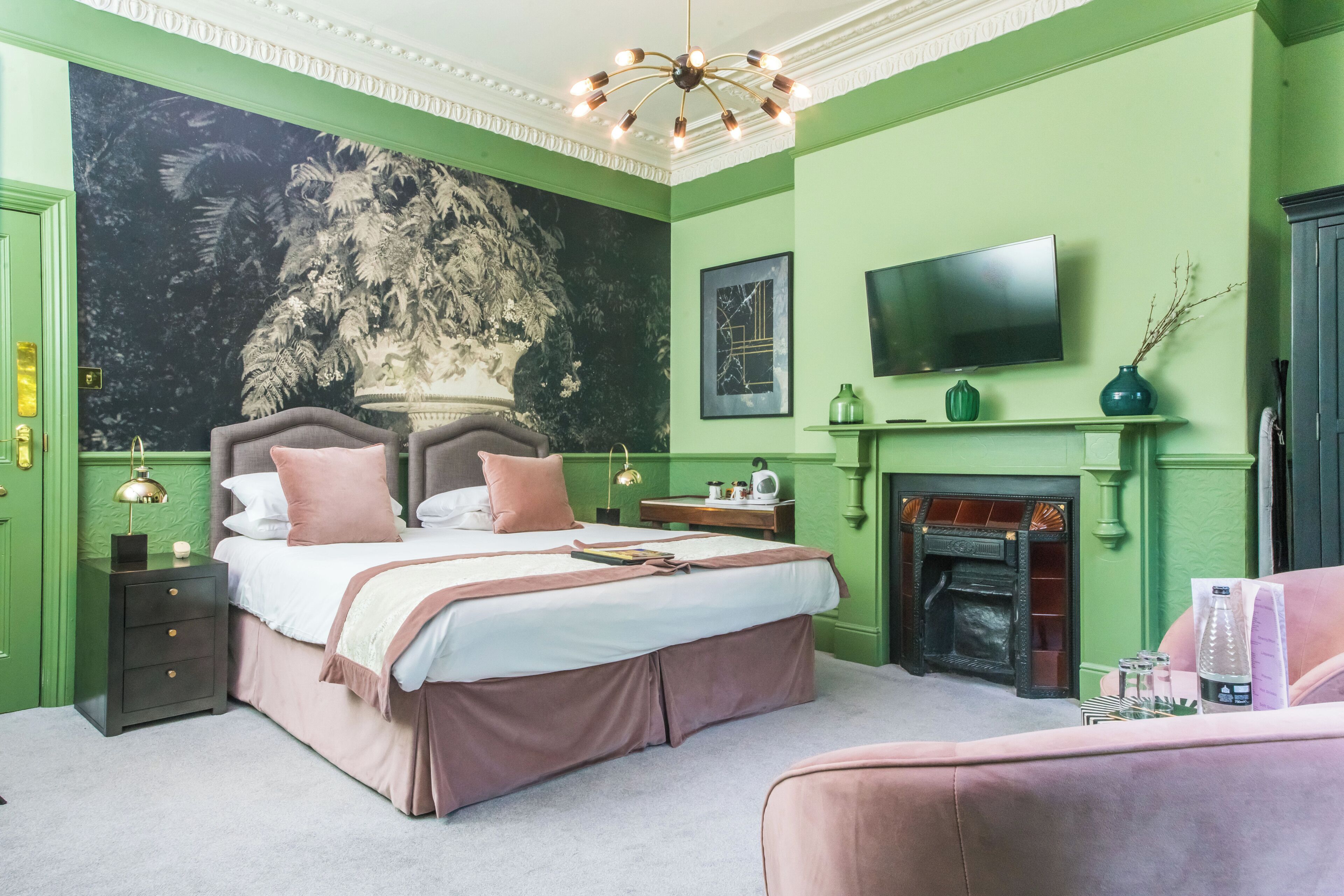 Um quarto com uma cama grande, televisão, lareira e uma parede verde.