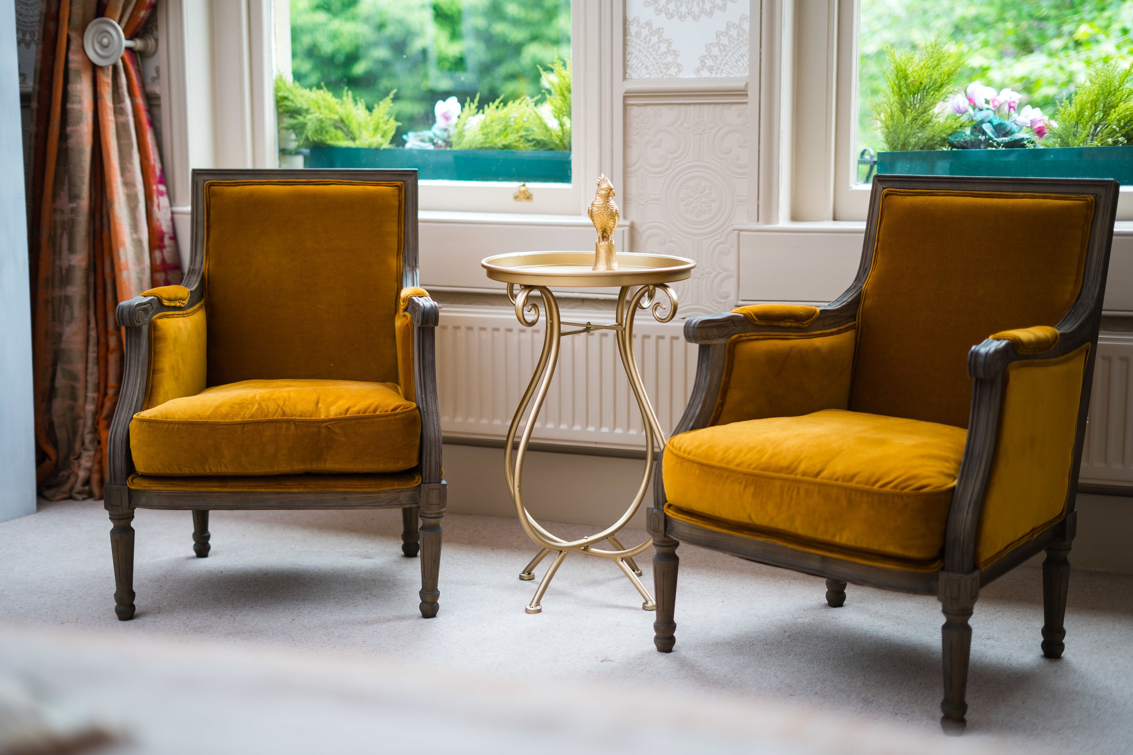 Two yellow armchairs with a small round table between them, positioned near a window with a view of greenery.