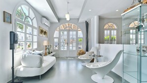 Un interior moderno con un sofá blanco, un aparador de vidrio y una zona de comedor con una silla y una mesa blancas.