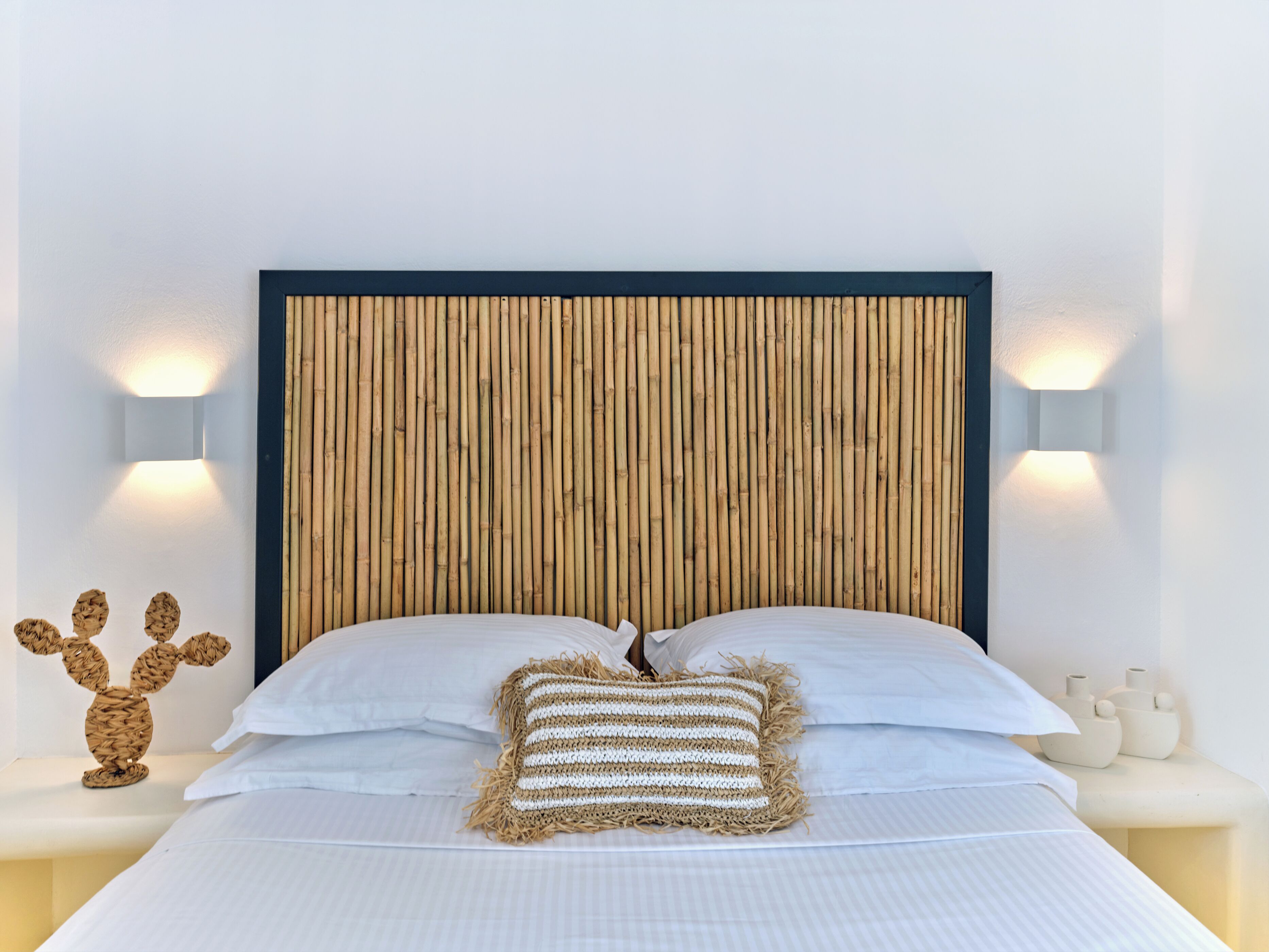 Ein Bett mit weißer Bettwäsche, einem gewobenen Kopfteil, zwei Wandleuchten und einem dekorativen Wandbild.