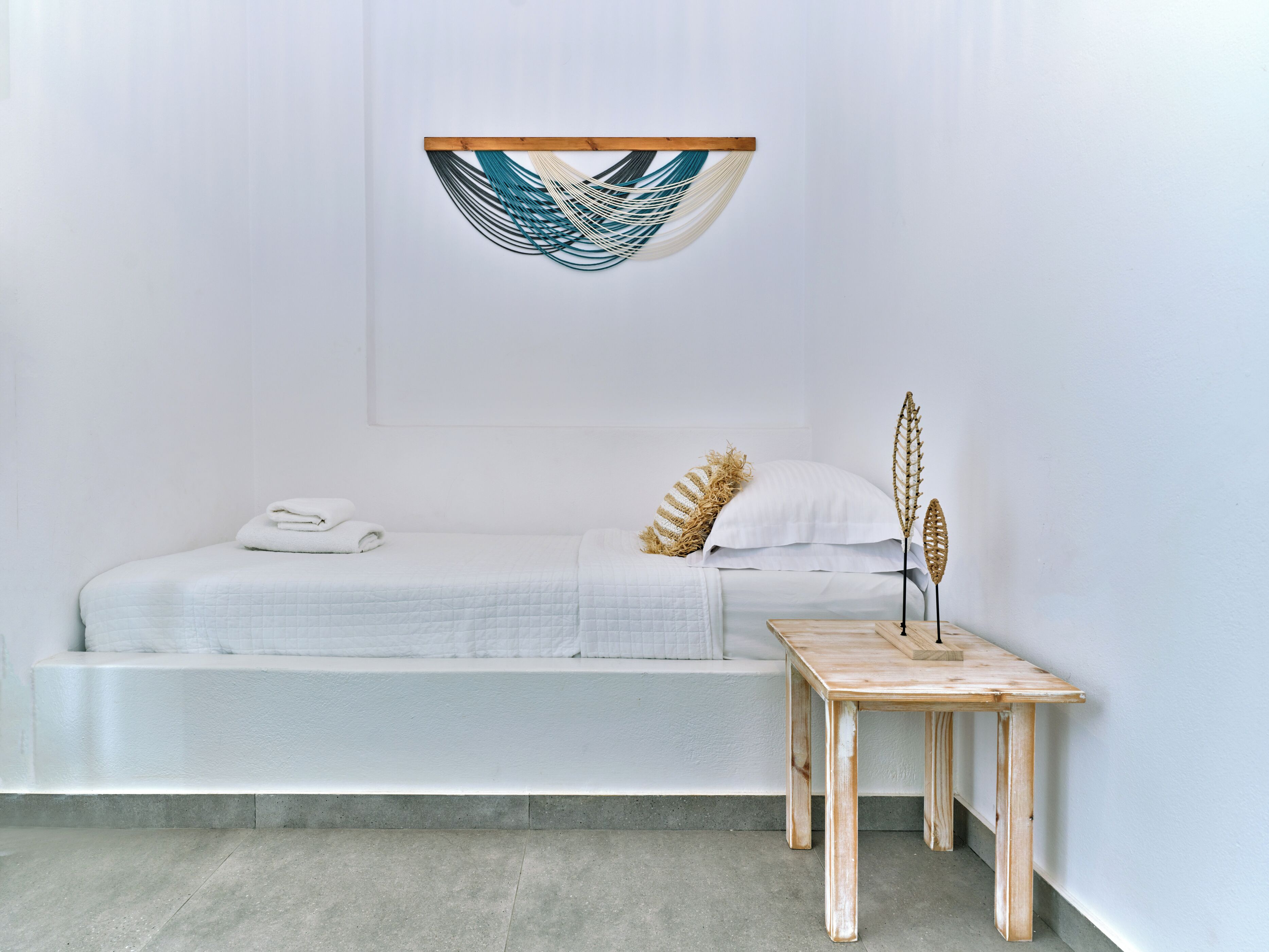 A minimalist bedroom with a bed, a small wooden table, and a wall-mounted decorative piece.