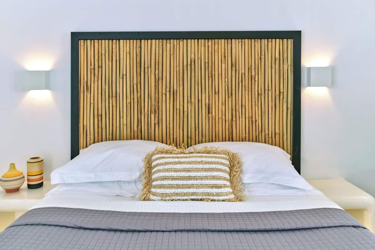 Un lit avec une tête de lit en bambou, une literie blanche et deux appliques murales.