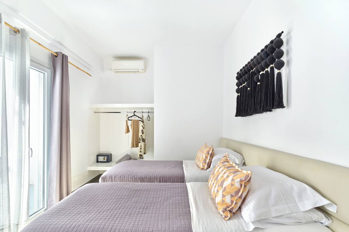Une chambre d’hôtel avec deux lits, une armoire, un miroir et un climatiseur fixé au mur.