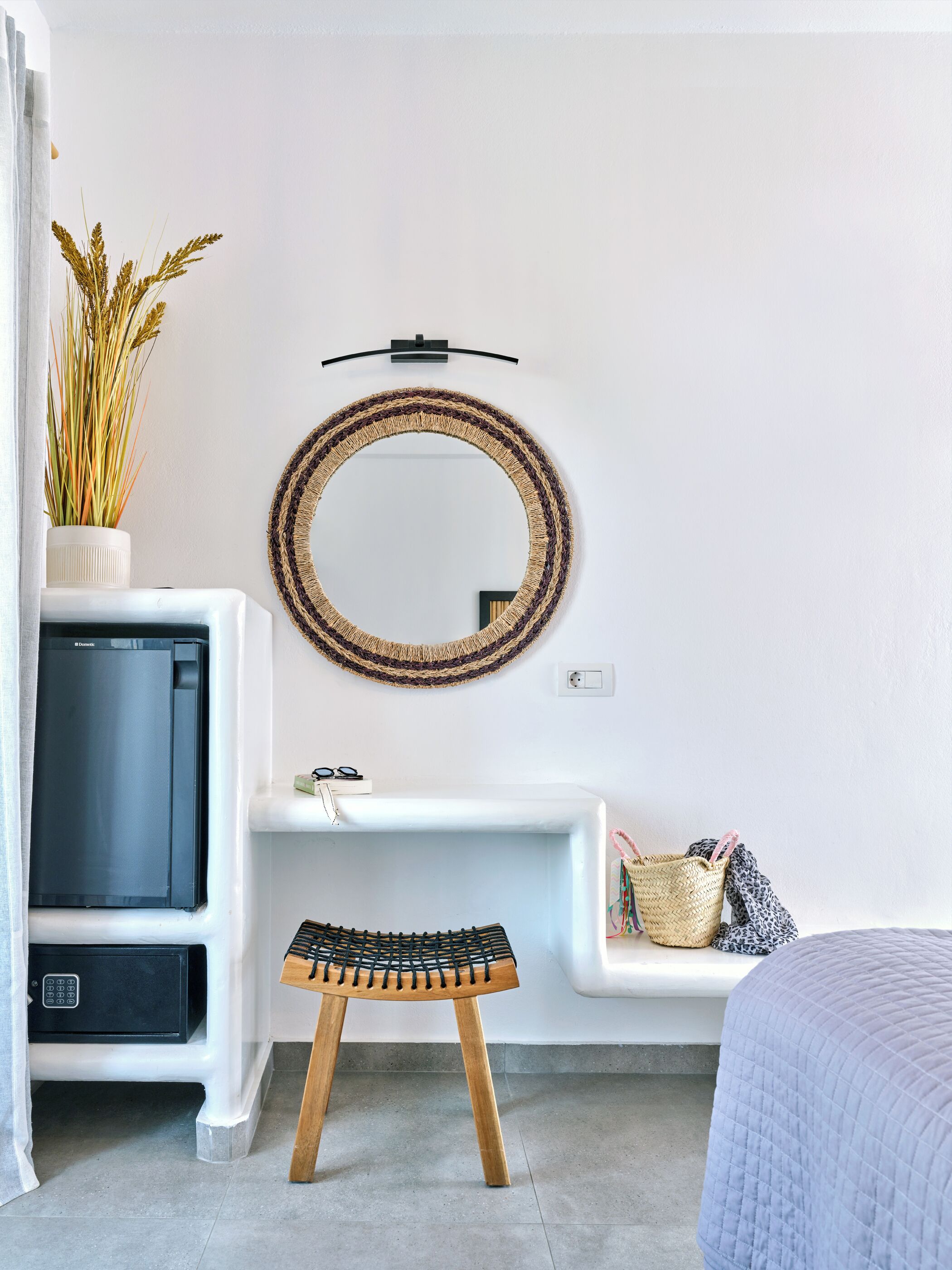 Een moderne badkamer met een witte wastafel, een ronde spiegel, een klein krukje en een mand.