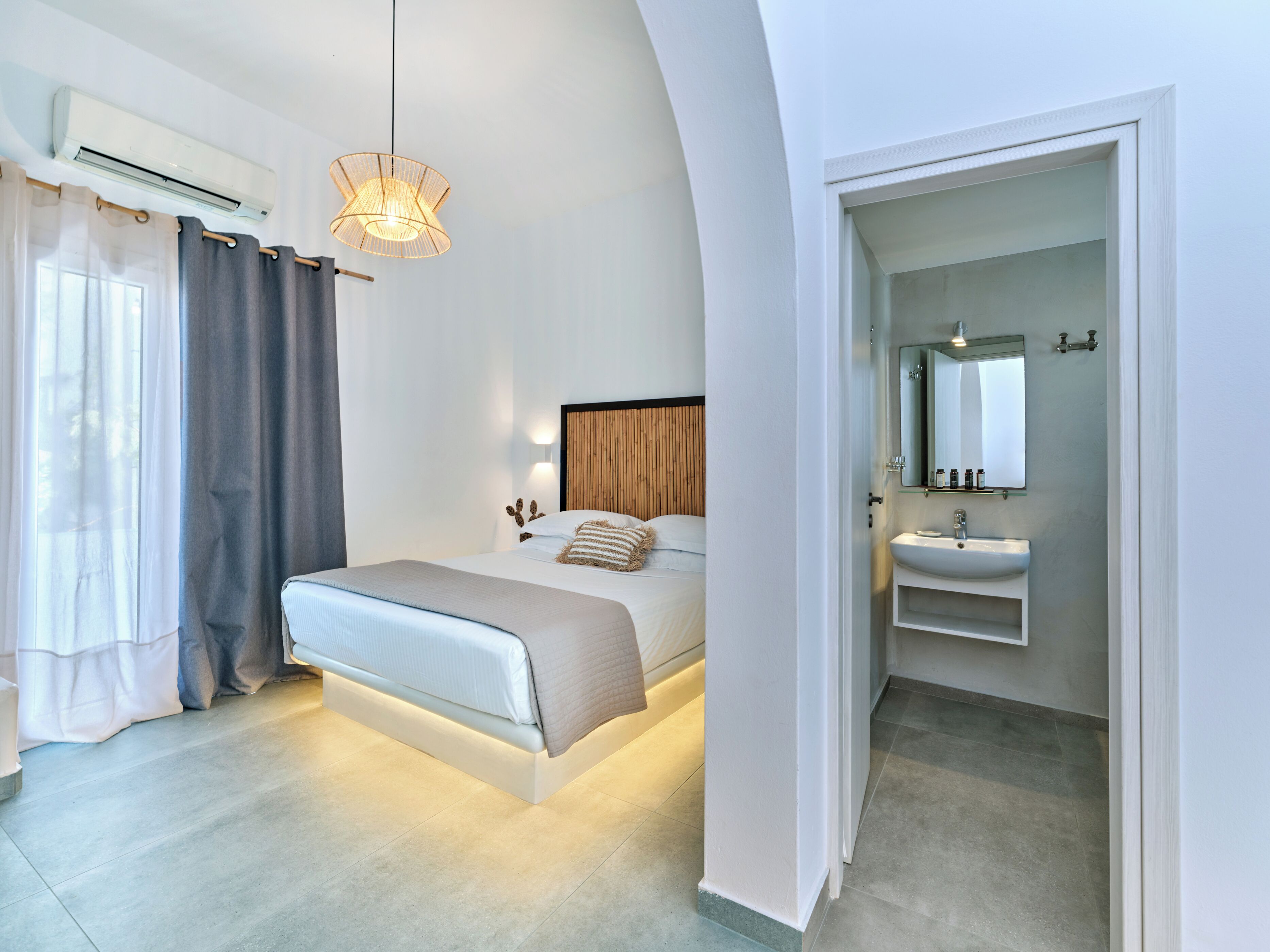 Une chambre à coucher moderne avec un lit, une table de chevet et une salle de bain équipée d’un lavabo et d’un miroir.